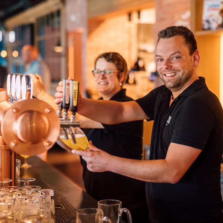 Zwei Mitarbeiter zapfen Bier an einer Theke.