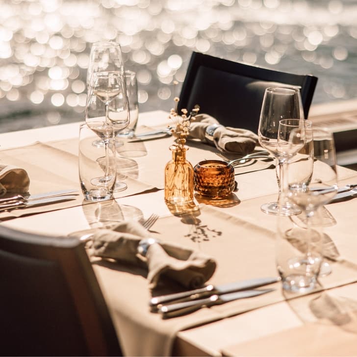 Eleganter gedeckter Tisch mit Seeblick im Hintergrund.