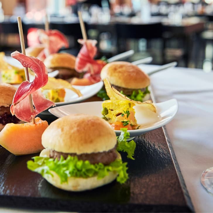 Vorspeisenplatte mit Mini-Burgern und Champagnergläsern auf Tisch.