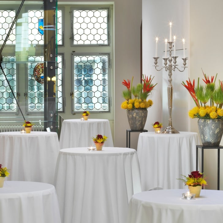 Stehtische mit weissen Tischdecken und Blumenarrangements in einem eleganten Raum.