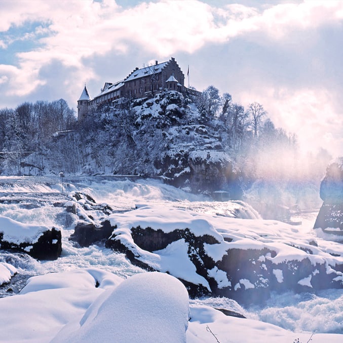 Schloss und Flusslandschaft im Schnee bei Sonnenuntergang.