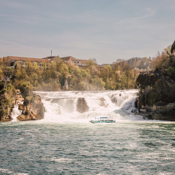 Rheinfall mit Boot inmitten sprudelndem Wasser und bewaldeter Umgebung.
