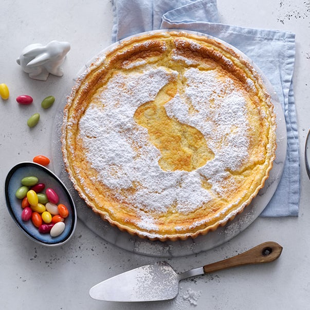 Zitronenkuchen mit Hasenmotiv, Ostereiern und Geschirr auf Tisch.