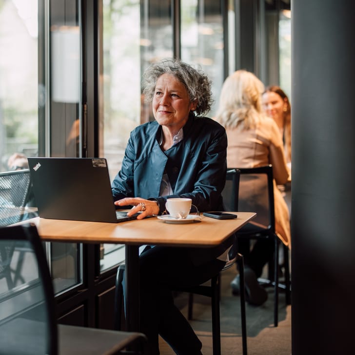 Person arbeitet lächelnd am Laptop in einem Café am Fenster sitzend.