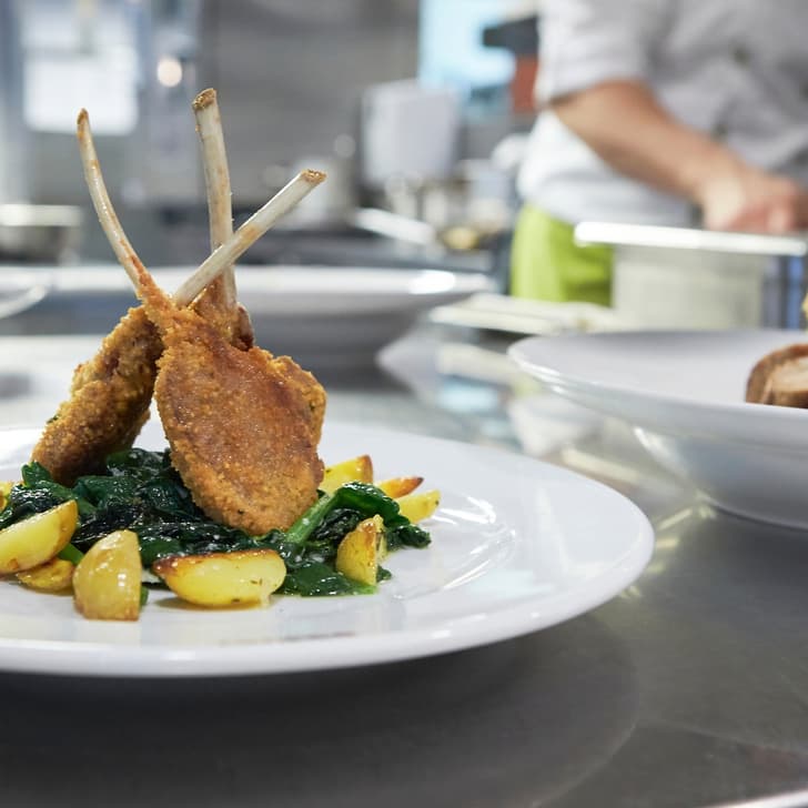 Gericht mit Lammkoteletts und Kartoffeln auf Teller in Küche.