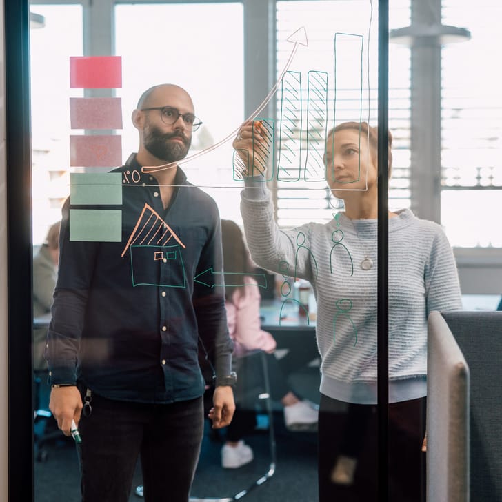 Menschen zeichnen Diagramme auf Glaswand im Büro.
