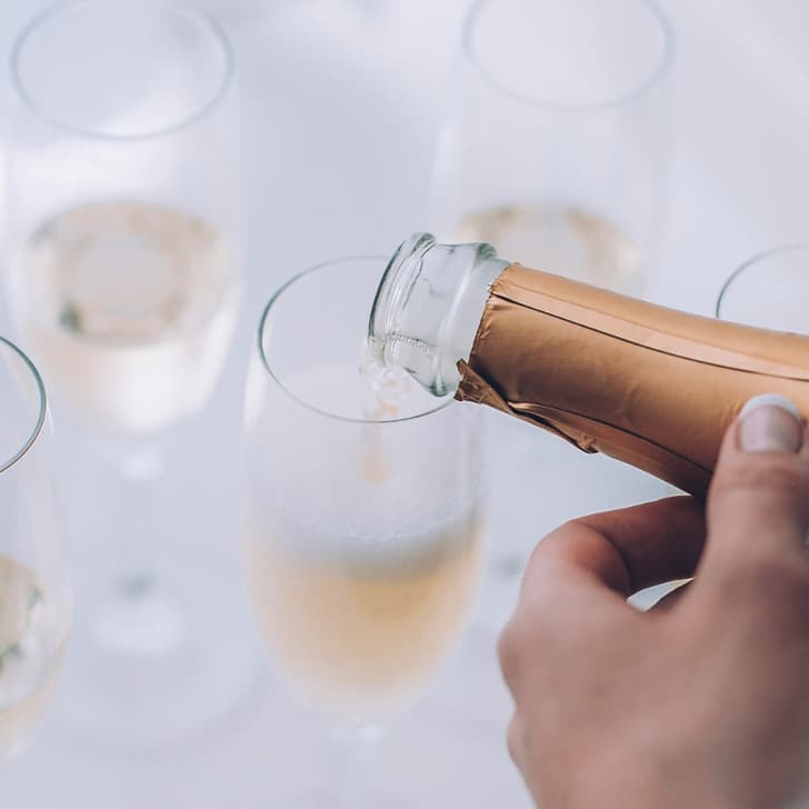 Person schenkt Sekt in ein Glas ein, mit weiteren Gläsern im Hintergrund.