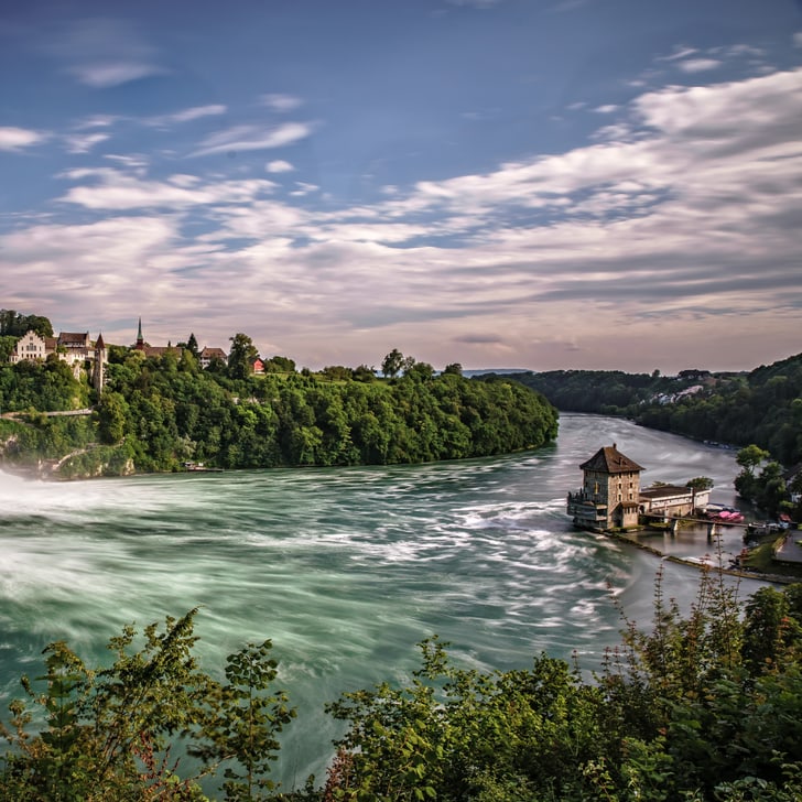 Ein grosser Wasserfall umgeben von grünem Wald und einem Gebäude.