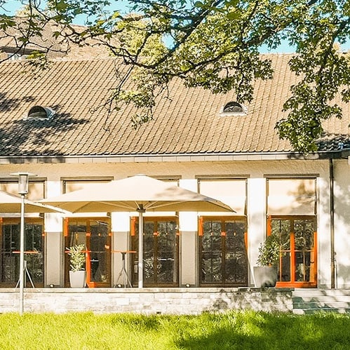 Gebäude mit Terrasse und Sonnenschirmen, von Bäumen umgeben.