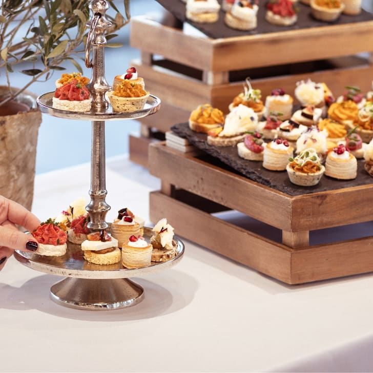 Hand greift nach einer Etagere mit Canapés auf Tisch mit Snacks.