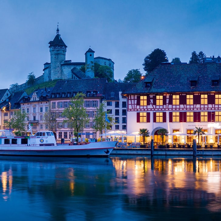 Historische Gebäude und Boote am Flussufer bei Nachtbeleuchtung.