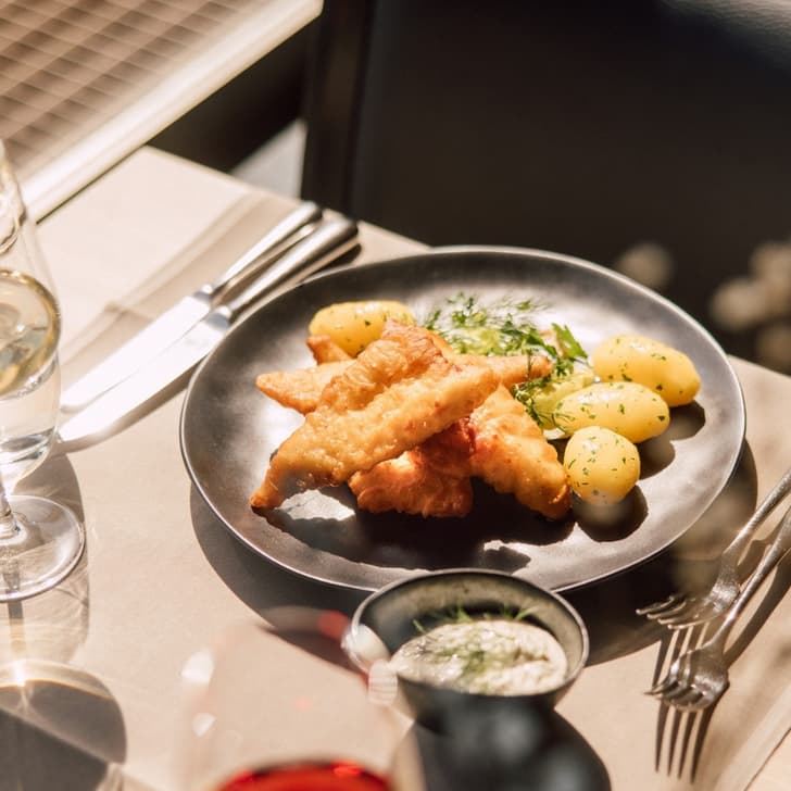 Gericht mit Fischfilets und Kartoffeln auf einem Tisch mit Weingläsern.