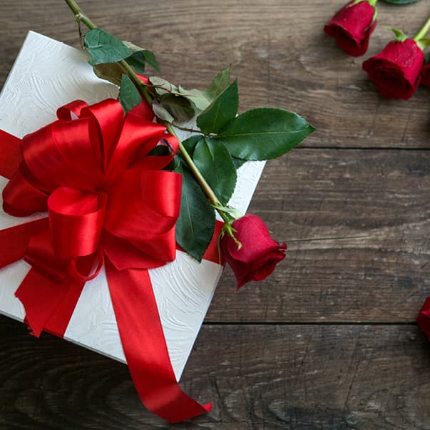 Geschenkbox mit roter Schleife und Rosen auf Holztisch.