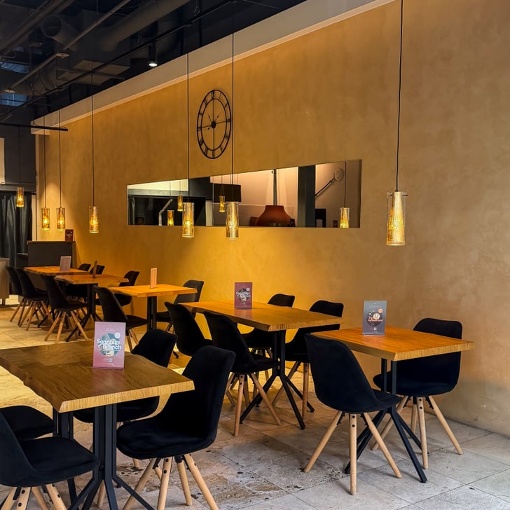 Gemütliches Café mit Holztischen und Stühlen, hängende Lampen.