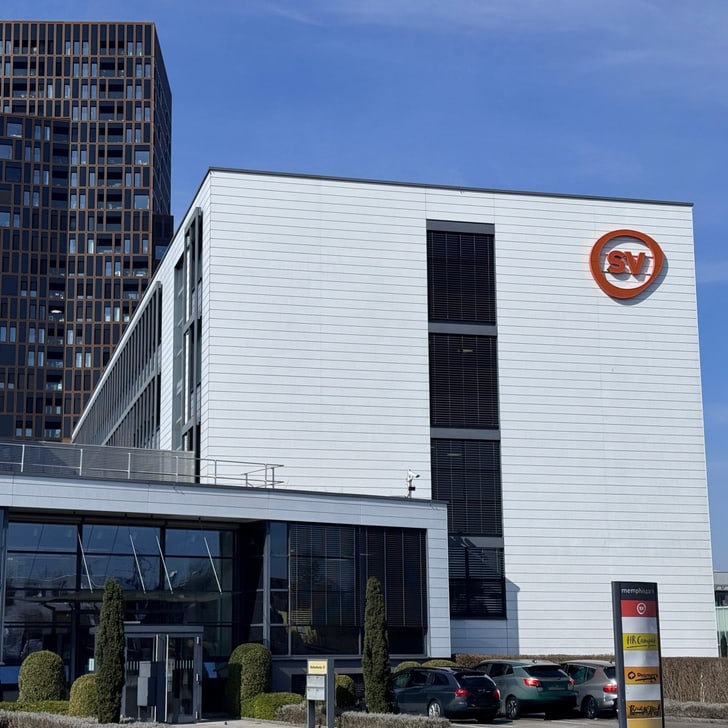 Weisses Gebäude mit SV-Logo und modernem Turm im Hintergrund.