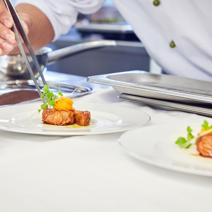 Koch richtet Gourmetgericht mit Pinzette an.