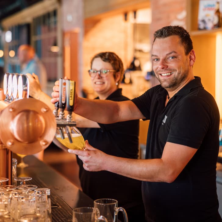 Zwei Mitarbeiter zapfen Bier an einer Theke.