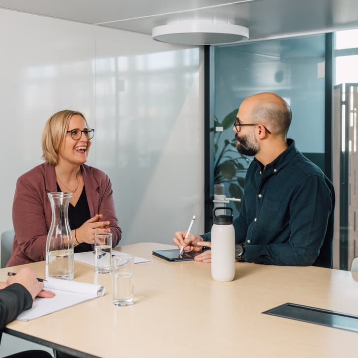 Drei Personen unterhalten sich in einem Besprechungsraum am Tisch sitzend.