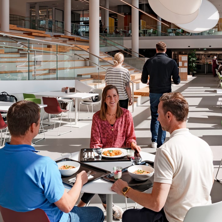 Drei Personen essen an einem Tisch in einem modernen Café.