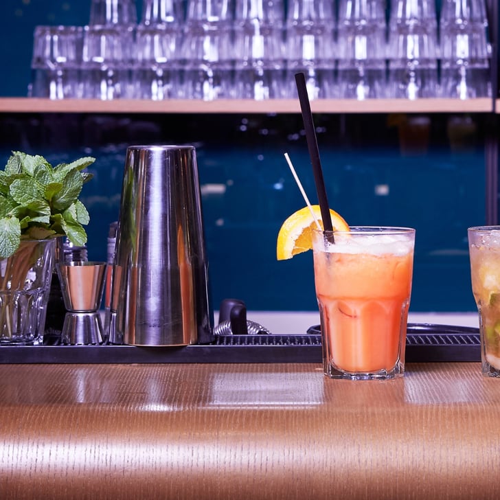 Zwei Cocktails auf einer Bar mit Chips und Minze im Hintergrund.