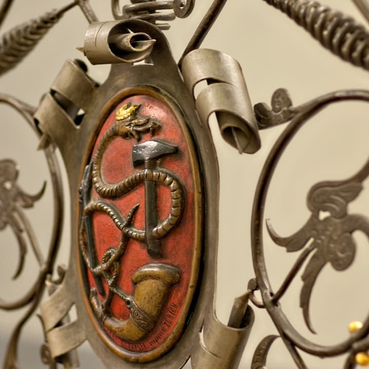 Nahaufnahme eines verzierten Metalltors mit rotem Wappenmotiv.