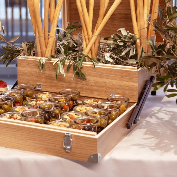 Essenspräsentation mit kleinen Gläsern und Olivenzweigen auf Tisch.