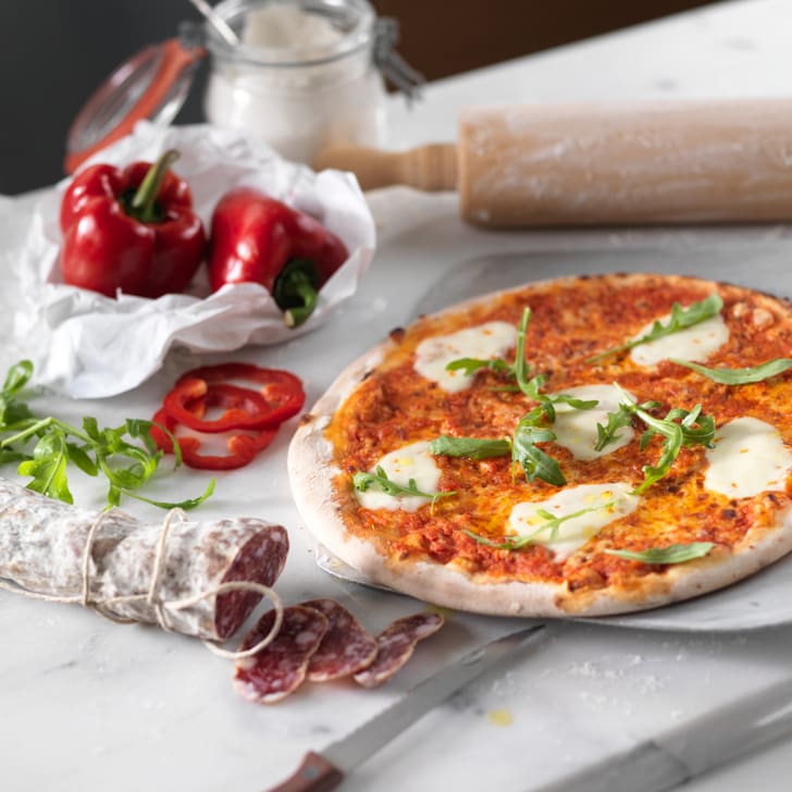 Pizza auf Marmor mit Peperoni, Salami und Nudelholz.