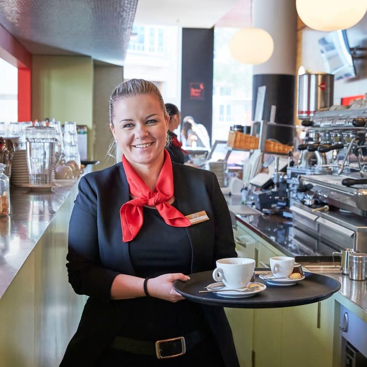 Kellnerin mit Tablett in einem Café mit Espressomaschine.