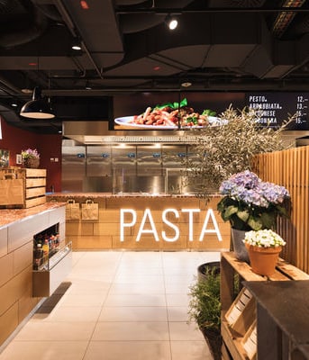 Innenansicht eines modernen Restaurants mit Pflanzen und Bildschirmen.