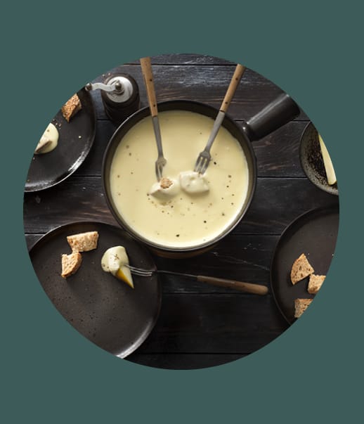 Topf mit Käsefondue und Brotstücken auf Tellern.