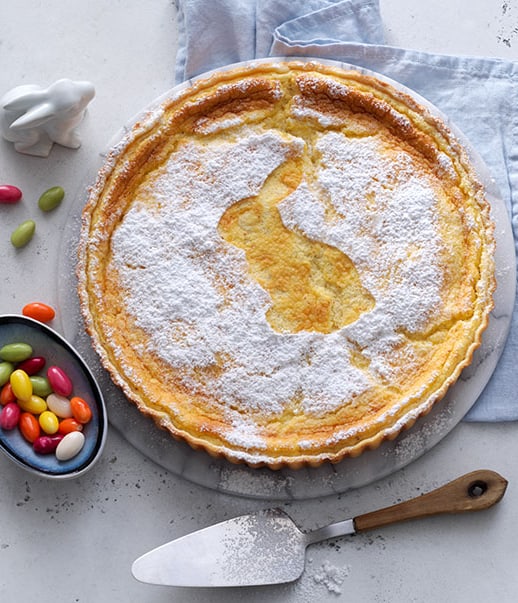 Zitronenkuchen mit Hasenmotiv, Ostereiern und Geschirr auf Tisch.
