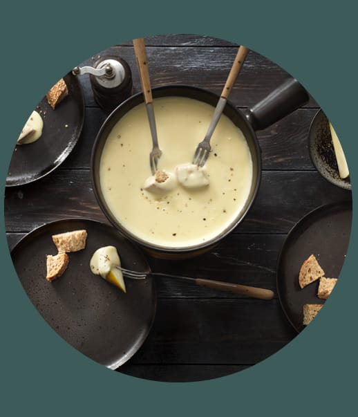 Käsefondue mit Brotstücken auf Tellern.