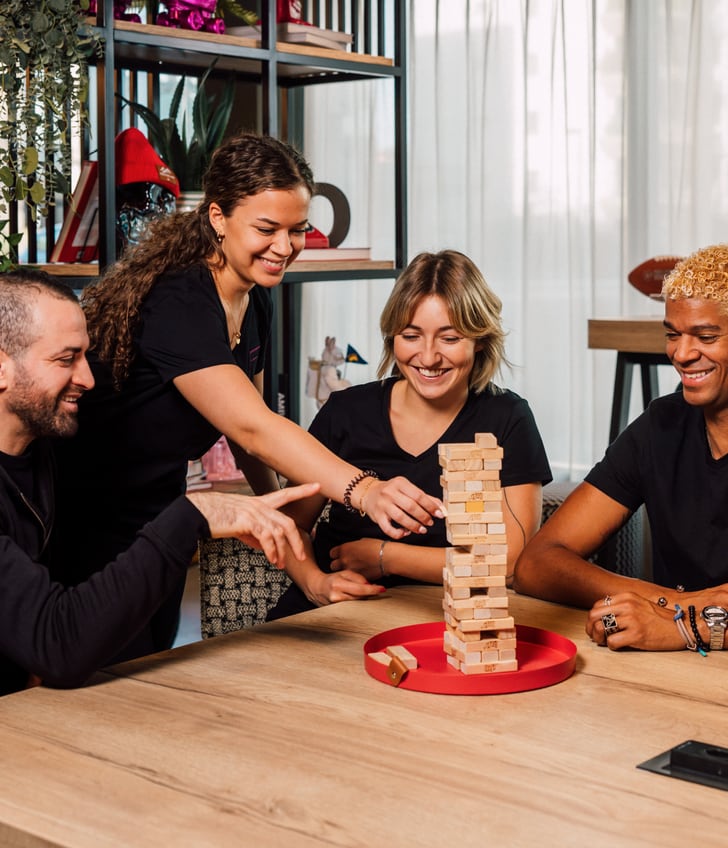 Vier Personen spielen Jenga-Steinspiel am Tisch.