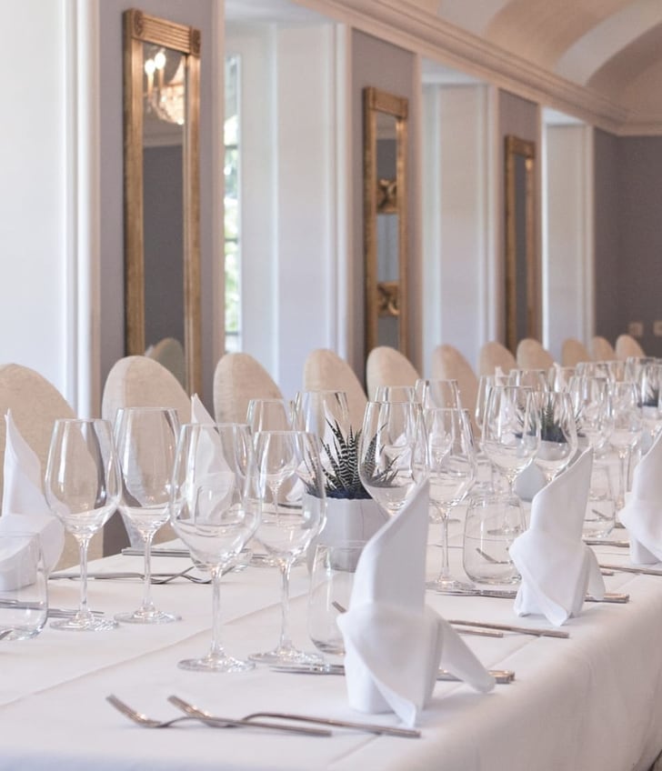 Eleganter, gedeckter Tisch in einem Festsaal mit Spiegeln und Kronleuchtern.