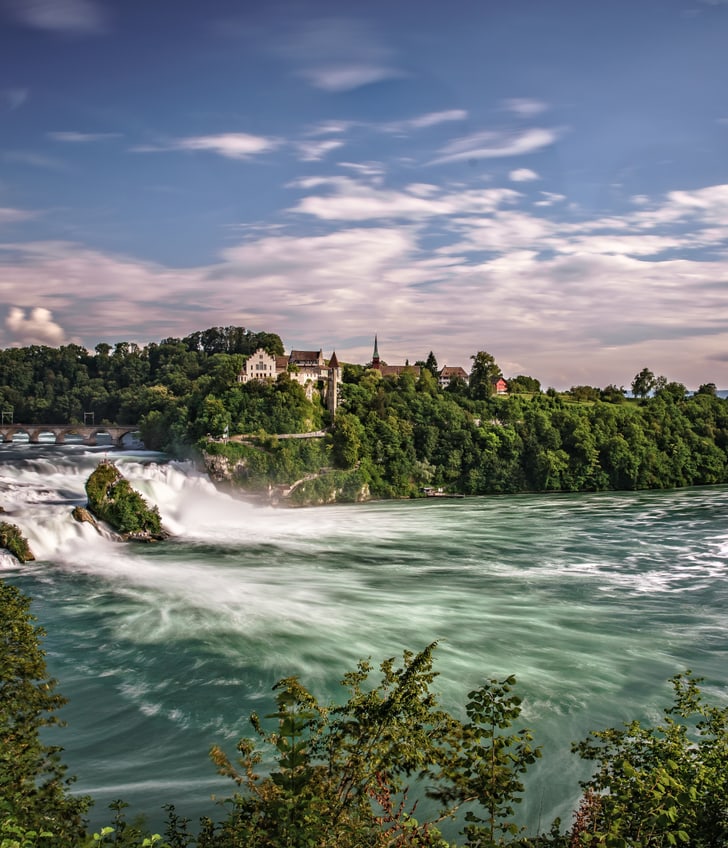 Landschaft mit grossem Wasserfall und bewaldeten Ufern.