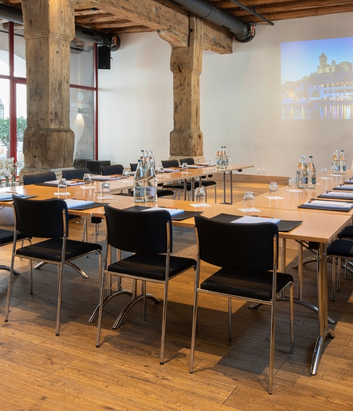 Konferenzraum mit Holzboden und Projektionsfläche.