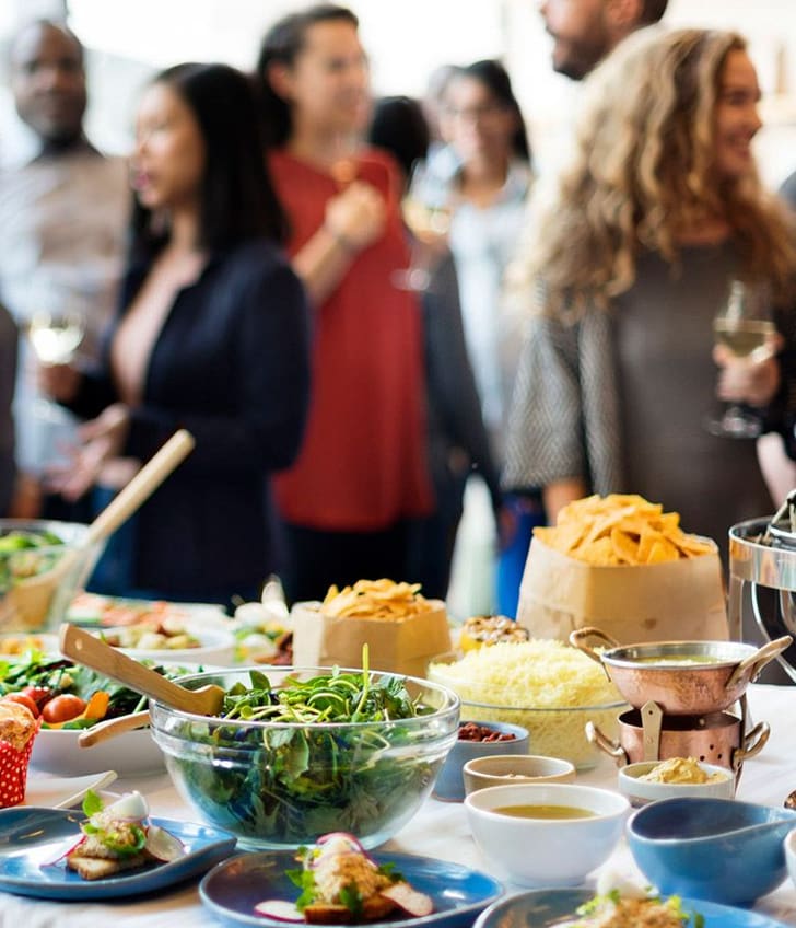 Buffet mit verschiedenen Speisen und Menschen im Hintergrund bei einer Veranstaltung.