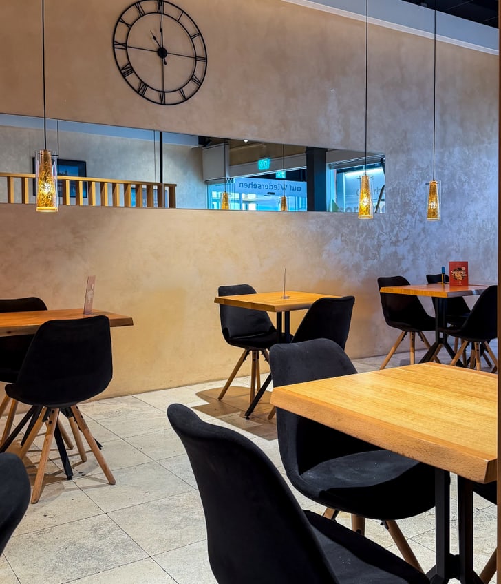 Leeres Café mit Holztischen und schwarzen Stühlen.