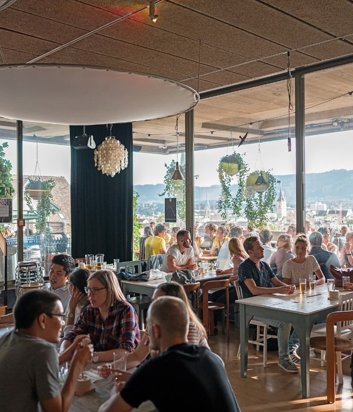 Menschen in einem Café mit Panoramafenstern und Aussenbereich.
