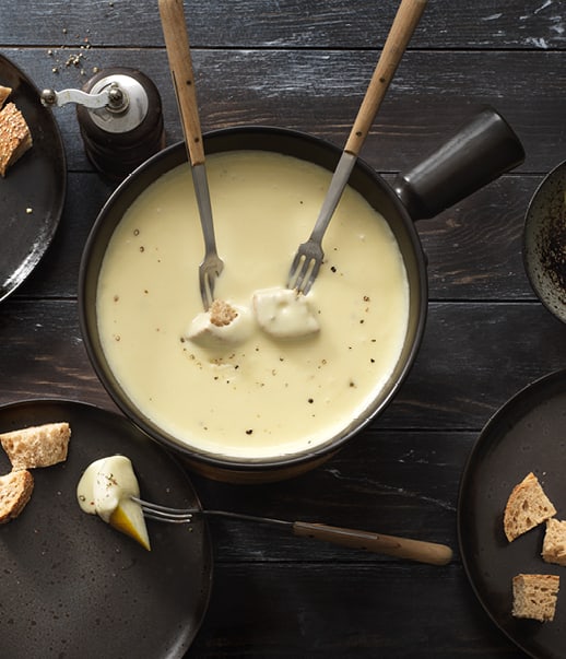 Käsefondue mit Brot und Birnen auf dunklem Tisch.