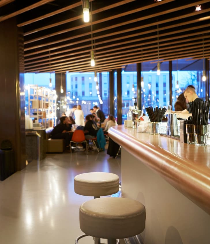 Moderne Bar mit langen Tresen, Sitzhockern und grossen Fenstern bei Abenddämmerung.