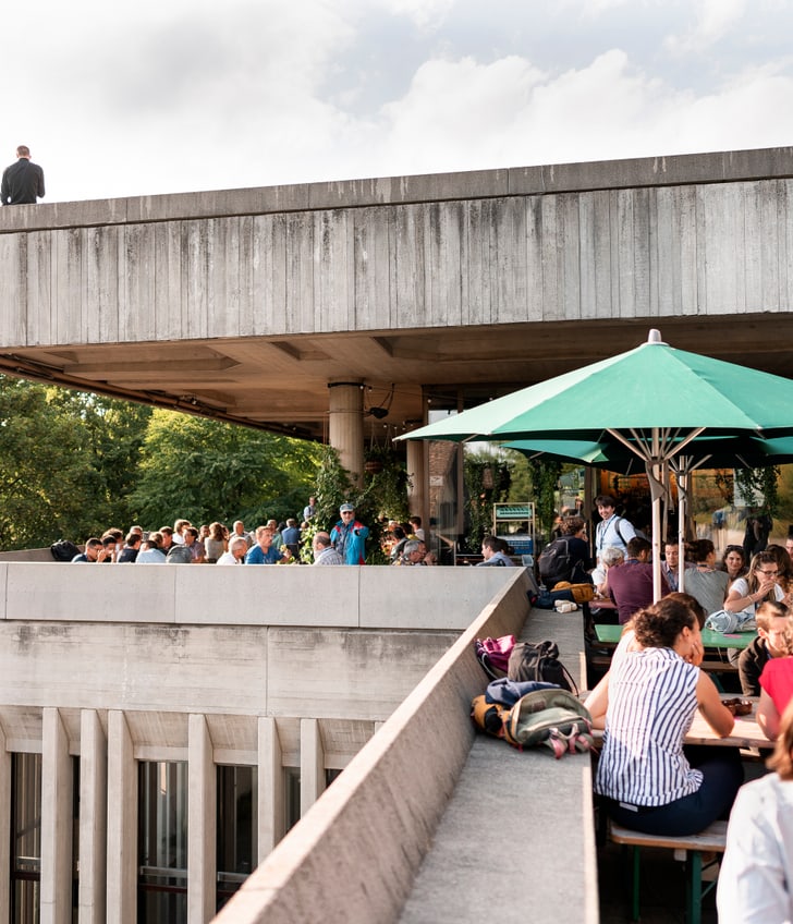 Menschen in einem Café auf einer Dachterrasse bei Sonnenschirmen.",