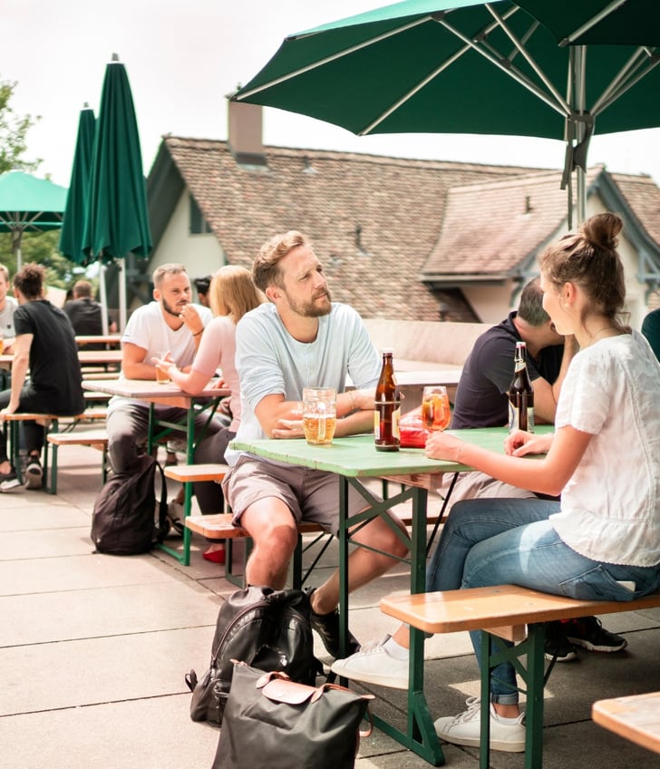 Menschen sitzen an Tischen im Freien mit Sonnenschirmen.",