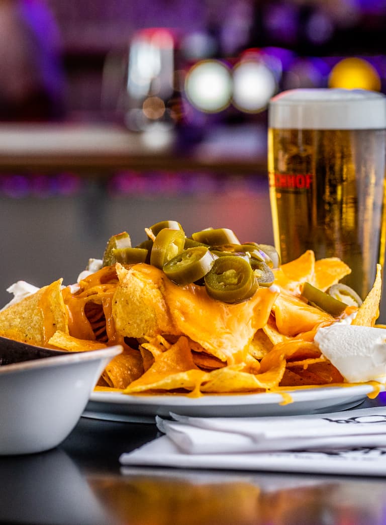 Nachos mit Jalapeños und Bier auf einem Tisch in einer Bar.