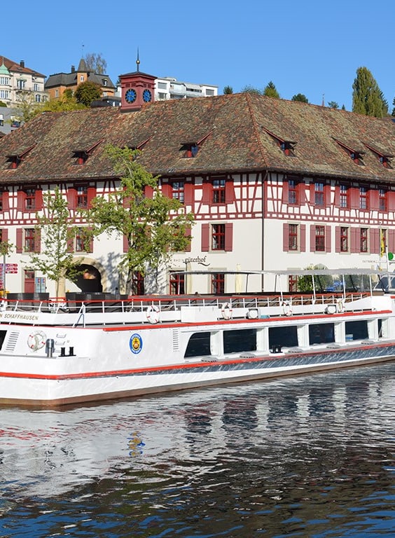 Weisses Boot an der Anlegestelle vor historischem Gebäude am Wasser.