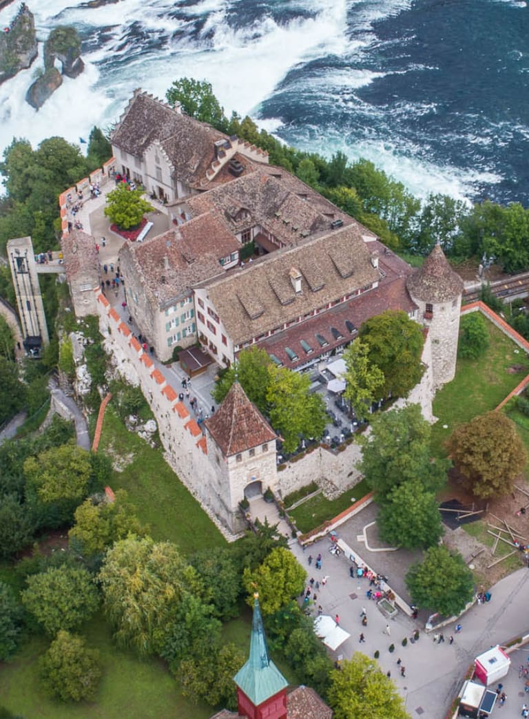 Luftbild eines Schlosses am Fluss mit Wasserfällen und einer Brücke.