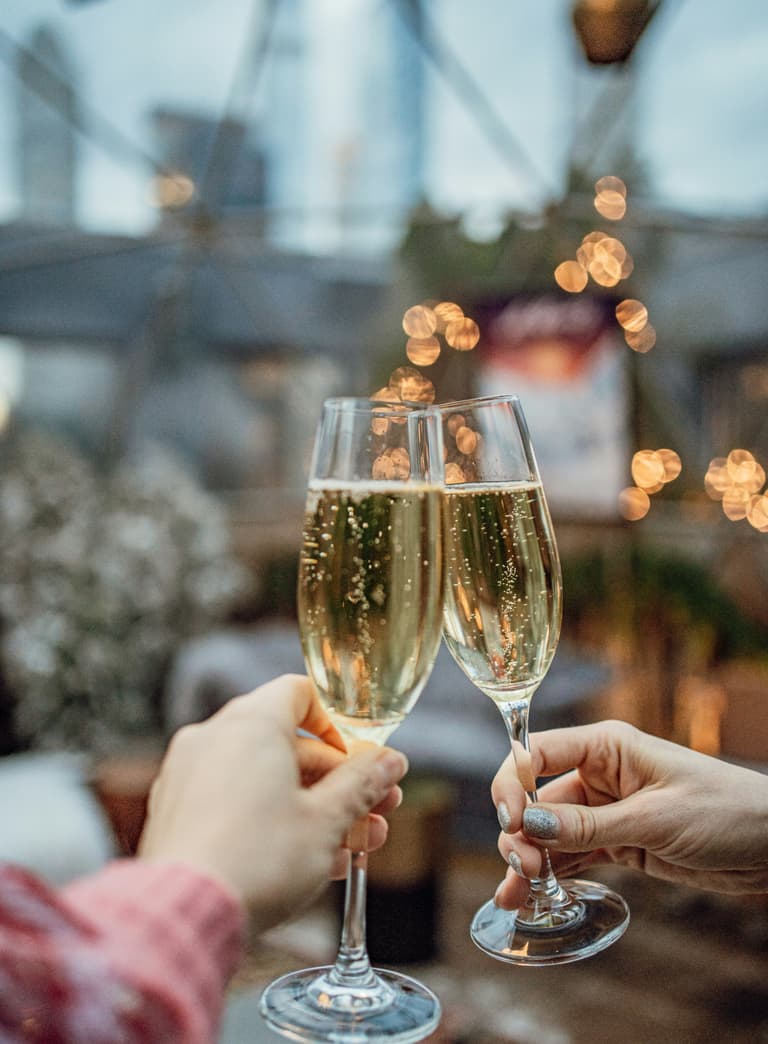 Zwei Personen stossen mit Sektgläsern an, unscharfer Hintergrund.