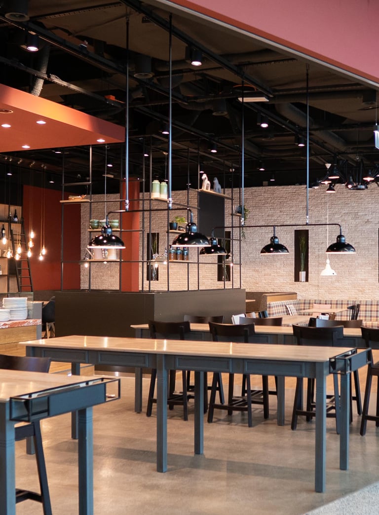 Leeres Restaurant mit Holz- und Metallmöbeln, hängende Leuchten.