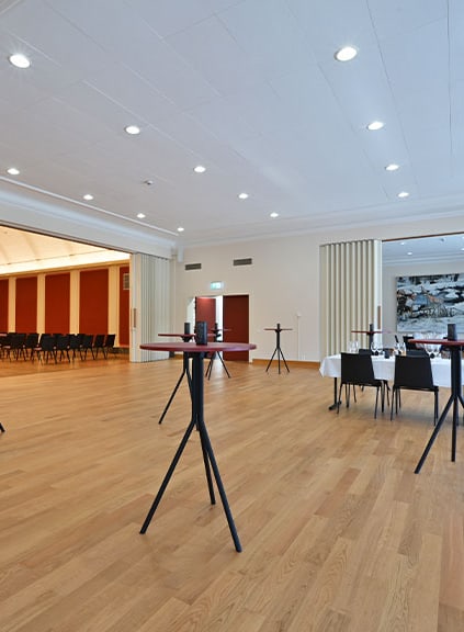 Grosser Veranstaltungssaal mit Holzboden und Stehtischen.