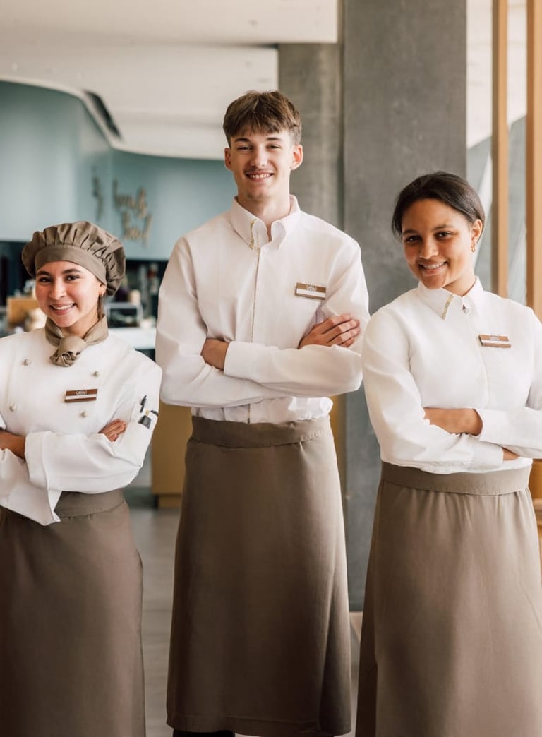 Drei Restaurantangestellte in Uniformen stehen mit verschränkten Armen im Speisesaal.